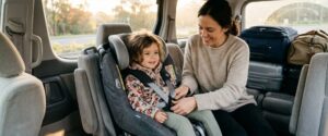 Parent securing a child into a car seat inside an airport shuttle with child seat Sydney families can book